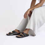 Sandalias Birkenstock Mogami Terra Stealth Birko-Flor Black, calzado por modelo femenino sentada, cuerpo entero de piernas